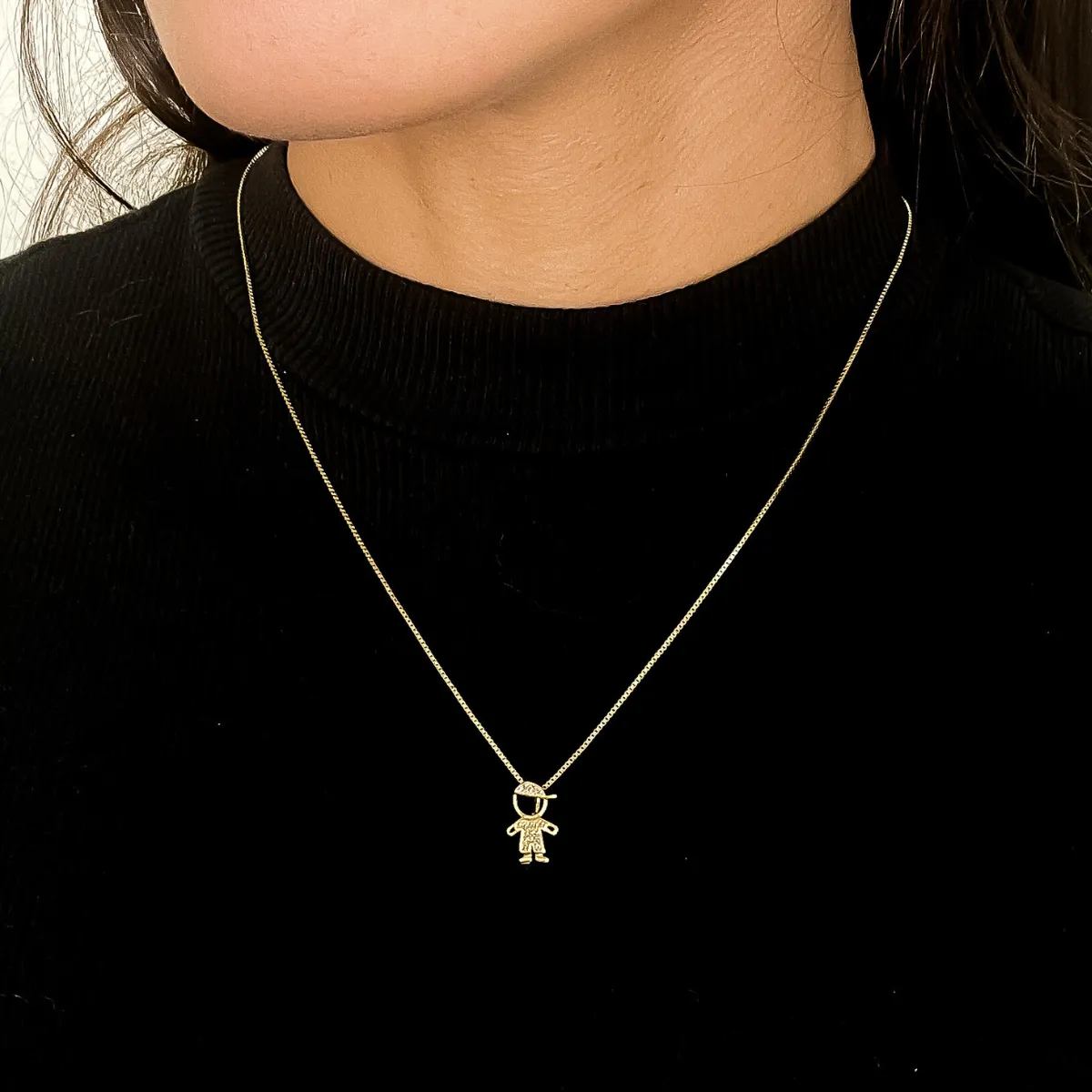 Colar delicado com símbolo de menino em ouro 18K, ideal para mães e avós, usado com blusa preta.